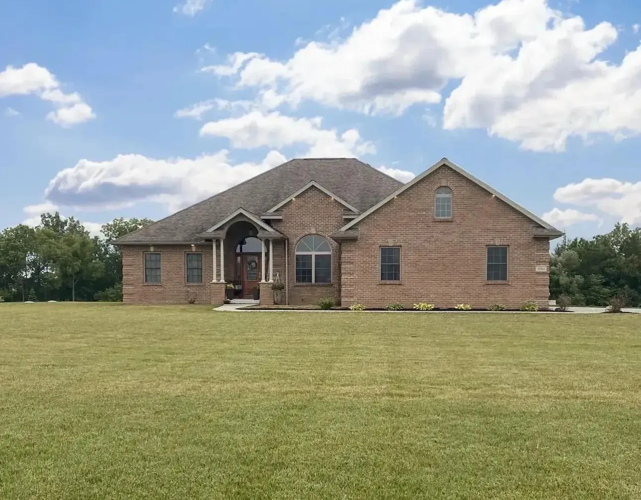 custom home with brown brick in the middle of a rural area.