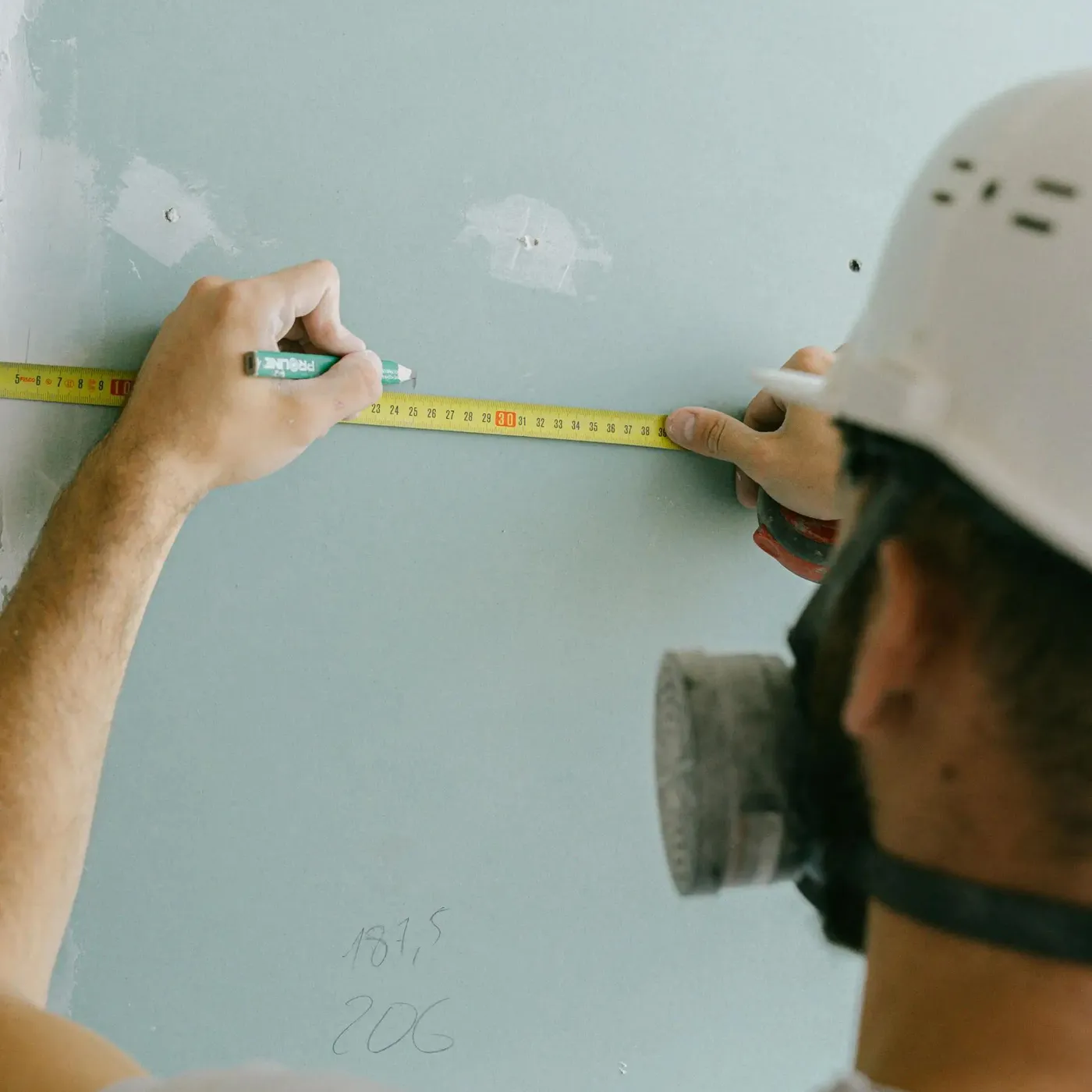 worker repairing drywall by marking where patches need to go