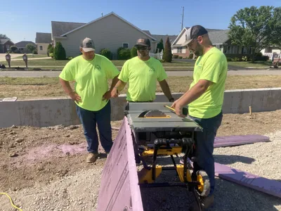 three construction workers measuring at a table saw