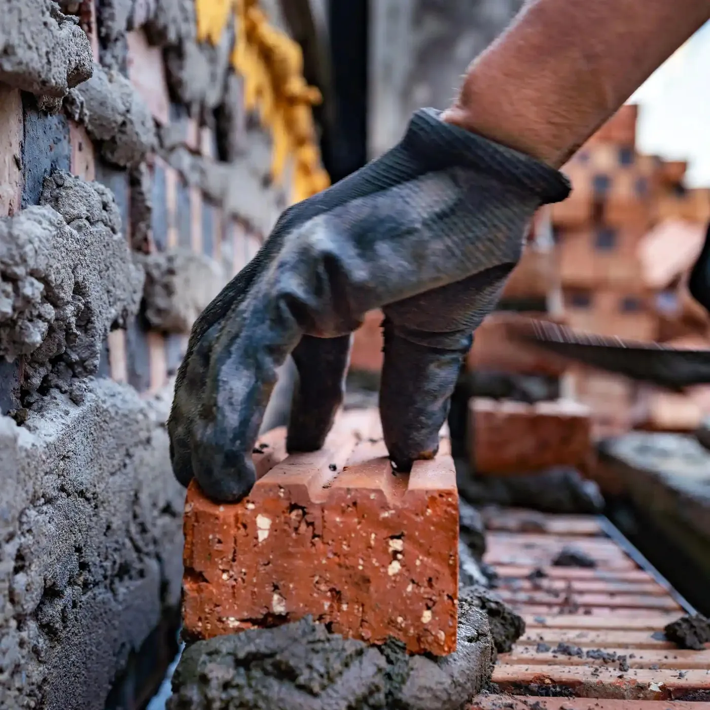 a gloved hand laying a brick on mortar